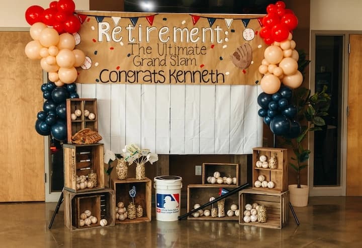 Baseball-themed retirement banner reading “Retirement: The Ultimate Grand Slam Congrats Kenneth,” with a pinstripe backdrop, balloon pillars, and baseball props.