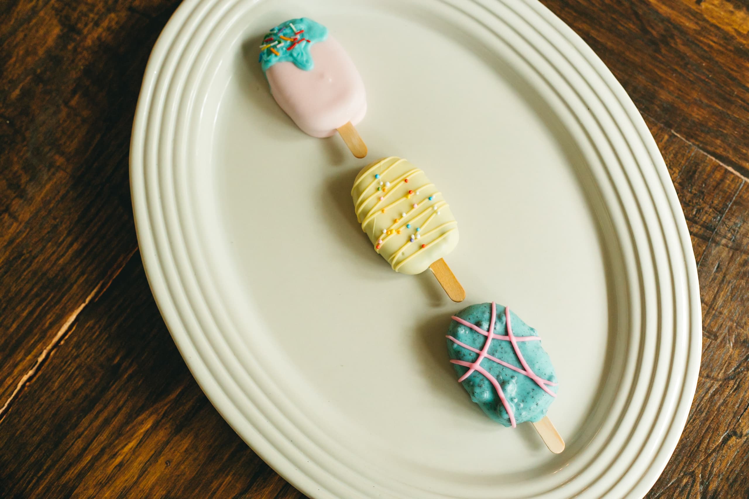 An angled view of the pink, yellow, and turquoise cakesicle trio on a wood table.