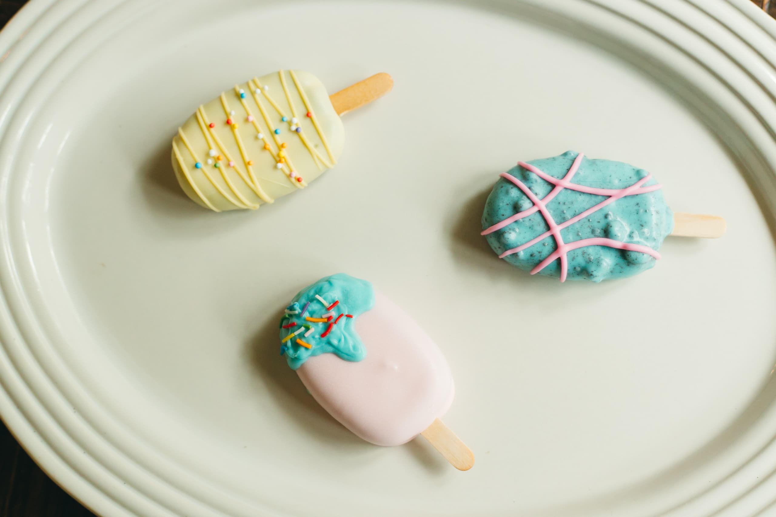 A closer view of the pink, yellow, and turquoise cakesicle trio arranged in a triangle on a white plate.