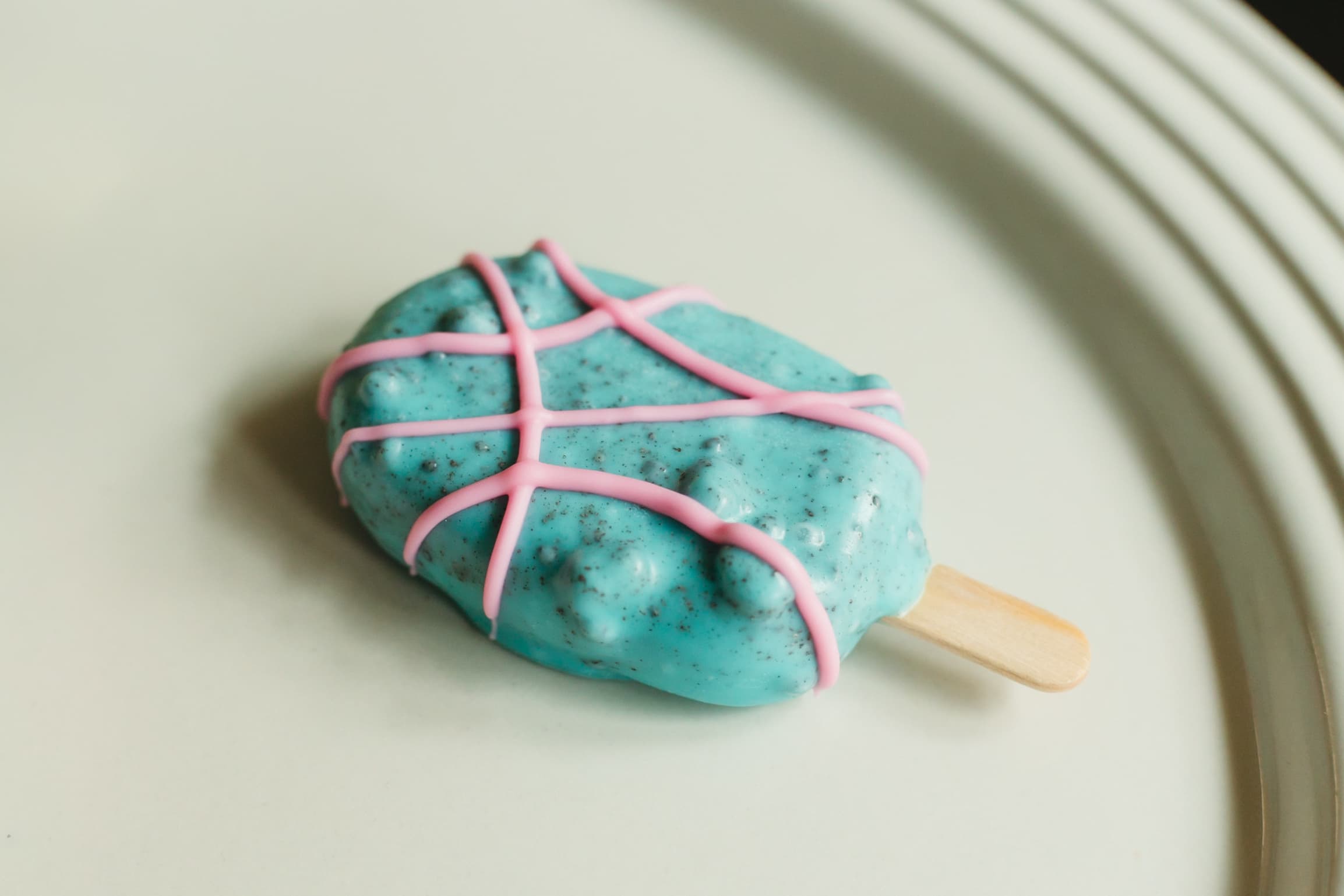 Close-up of a turquoise cakesicle with pink piped crisscross lines.
